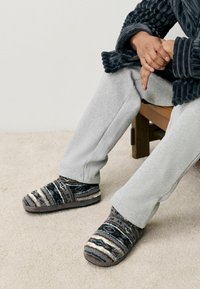 Gezellige instap slippers met een textuur gebreide patroon in grijs, bruin en wit. Zacht materiaal en gevoerde zolen zorgen voor comfort.