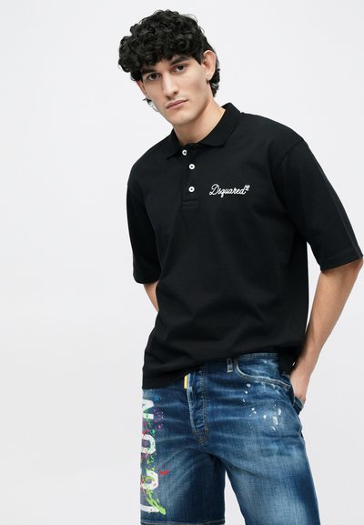 Mustast puuvillast polo särk, millel on kolm nööpi ja tikitud logo. Kandmiseks koos kulunud sinise teksapükste lühikestega, millel on värvilised plekid.