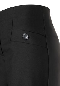 Nahaufnahme von schwarzen, maßgeschneiderten Hosen mit hoher Taille und einer kleinen, geknöpften Gesäßtasche.