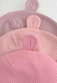 Drei gerippte Hüte in Lavendel, Pink und Hellpink, jeweils mit abgerundeten, ohrähnlichen Akzenten oben. Weicher Stoff, kreisförmiges Design.
