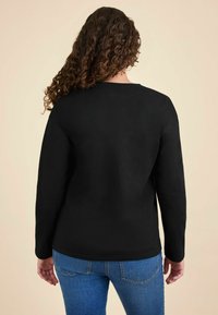 Maglietta nera a maniche lunghe con scollatura rotonda e una texture liscia, abbinata a jeans blu con tasche posteriori e una vestibilità aderente.