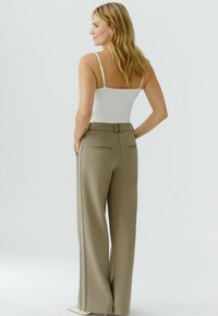 Hellbeige Hosen mit weitem Bein, vertikalen Streifen, strukturiertem Stoff und Gesäßtaschen, kombiniert mit einem schlichten weißen Tanktop.