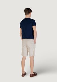 T-shirt à manches courtes marine associé à un short beige, affichant une coupe décontractée. Des chaussures en cuir marron complètent la tenue.