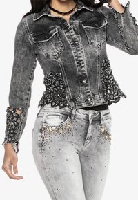 Musta kulutettu farkkutakki koristellulla pitsireunuksella, kahdella rintataskulla ja kuluneilla yksityiskohdilla. Harmaat farkut, joissa strassikoristeita.