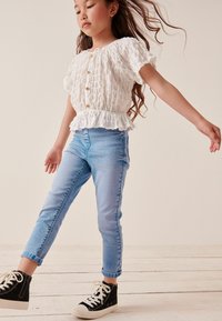 Vit, texturerad blus med puffärmar och framknappning, kombinerad med ljusblå skinnjeans och svarta högskaftade sneakers.