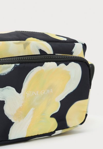 Black fabric bag with yellow floral design, featuring a smooth texture and a zip closure. "STINE GOYA" logo printed in white.