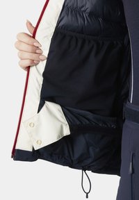 Navy and cream insulated jacket interior features a quilted texture, zippered pocket, and a mesh pocket, with a drawstring at the hem.
