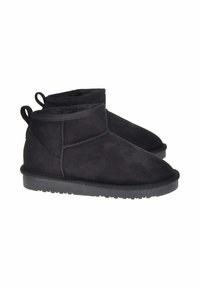 Stivaletti in suede neri a caviglia con forma arrotondata, suola piatta in gomma e dettagli cuciti lungo il bordo superiore. Presentano un tab di estrazione sul retro.