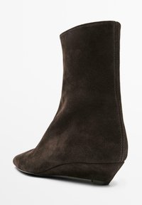 Brauner Wildleder-Stiefelette mit spitz zulaufender Kappe und Keilabsatz, mit glatter Textur und sauberen Nähten entlang der Kante.