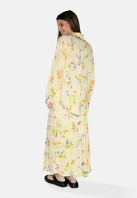 Vestito giallo leggero con motivo floreale, caratterizzato da maniche lunghe e una gonna fluida. Sandali neri completano il look.
