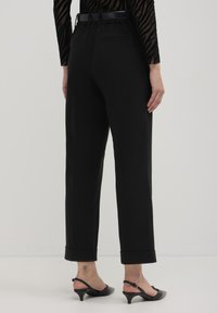 Pantaloni neri su misura con gamba dritta, orlo risvoltato e cintura elastica. Indossati con scarpe a sandalo nere.
