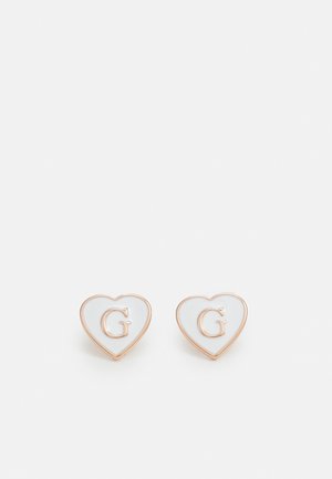 Boucles d'oreilles en forme de cœur avec bord doré, centres en émail blanc et lettre G en relief au centre sur fond blanc.