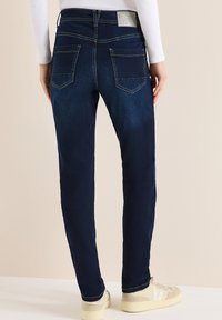 Jean skinny bleu foncé à texture lisse, design cinq poches et patch arrière de la marque. Présente des accents de coutures et une coupe ajustée.