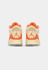 Las zapatillas de cuero en beige y naranja presentan un fondo texturizado, con una unidad Air visible y un logo de Jumpman en el talón.