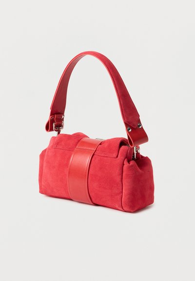 Κόκκινη σουέντ τσάντα με φαρδιά δερμάτινη κεντρική λωρίδα και χοντρό λουρί ώμου σε απλό ανοιχτό φόντο.