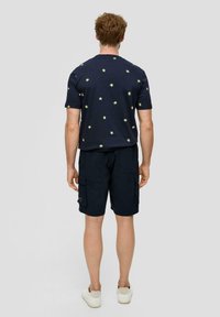 Granatowy t-shirt z żółtym nadrukiem palm, w połączeniu z granatowymi szortami cargo. Luźny design, krótkie rękawy i tenisówki.