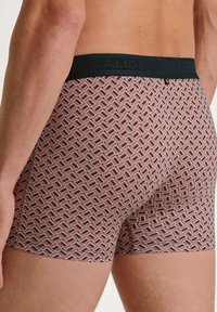 Herren-Boxerbriefs mit geometrischem Muster in Rot, Weiß und Schwarz. Der elastische Bund zeigt die Marke "CALIDA". Material aus Baumwollmischung.