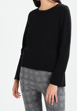 Schwarzer Strickpullover mit Rundhalsausschnitt und geripptem Saum, kombiniert mit grauen karierter Hose. Mit langen Ärmeln und lockerer Passform.