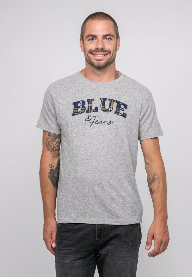 T-shirt en coton gris avec "BLUE & Jeans" imprimé en bleu foncé et motifs à carreaux. Manches courtes, col rond et coupe décontractée.