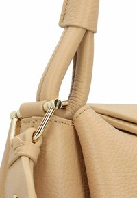 Beige leren handtas met een gestructureerd oppervlak, gladde handgrepen en gouden hardware op het bevestigingspunt, wat vakmanschap benadrukt.