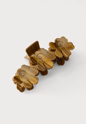 Pince à cheveux en plastique marron comportant trois sections en forme de fleur, chacune avec un centre circulaire, sur un fond clair et uni.