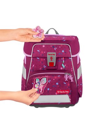 Lila Rucksack mit floralen Mustern, reflektierenden Streifen und Aufnähern. Eine Hand hält einen Blumenaufnäher in der Nähe eines Schmetterlingsaufnähers auf der Vorderseite.