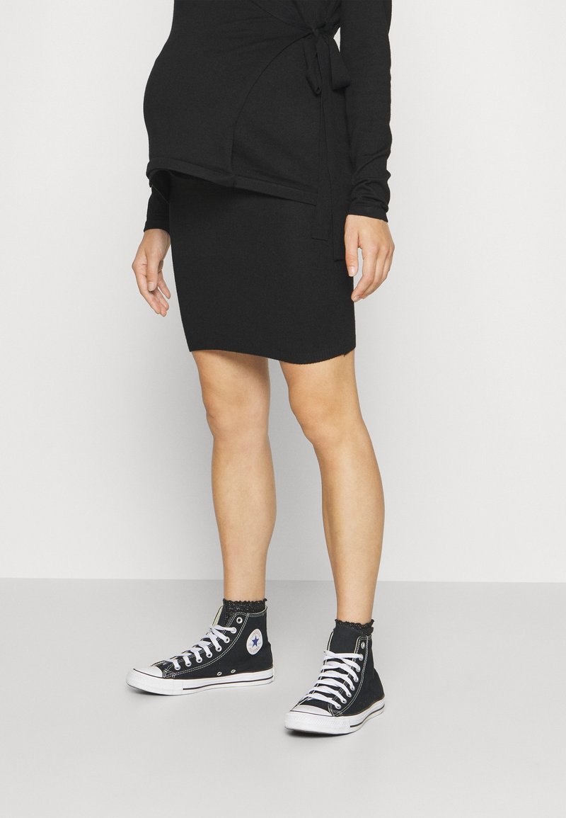 Svart långärmad topp med knyt i midjan, parat med en figurnära svart kjol och svarta högskurna sneakers med vita snören och en logotyp.