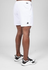 Witte sportshorts met een zwart logo, elastische tailleband en zijzakken. Gecombineerd met zwart-rode sneakers met een gestructureerde zool.