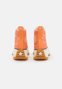 Kaanva orange kõrged sneakers tähtede aktsentidega, millel on valged õmblused ja paks kreemjas tald, mille all on kummist välispind.