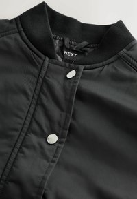 Schwarze gesteppte Jacke mit geripptem Kragen und zwei silbernen Druckknöpfen, innen am Kragen mit Markenlabel "NEXT".