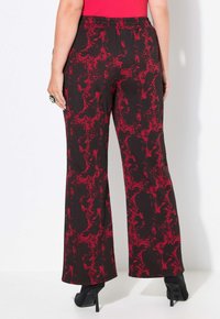 Schwarze weit geschnittene Hose mit einem roten abstrakten Muster und vertikalen Streifen. Aus strukturiertem Stoff gefertigt, mit einem taillierten Bund und gesäumten Kanten.