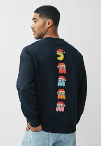 Felpa navy in cotone, con personaggi in pixel art dai colori rosso, blu, rosa e giallo sul retro. Collo a giro e polsini a coste.