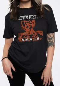 Black cotton t-shirt featuring a graphic print in orange and white, depicting a skeletal design with the text "OFFSPRING SMASH."
