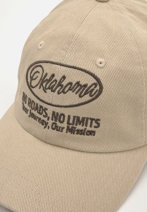 Béžová kšiltovka vyrobená z texturované látky, s hnědým vyšitým nápisem "Oklahoma" a frází "ŽÁDNÉ CESTY, ŽÁDNÁ OMEZENÍ."