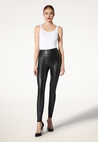 Collant neri a vita alta realizzati in un materiale lucido e morbido, abbinati a un top bianco attillato e tacchi alti neri.