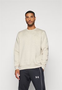 Sweatshirt bej deschis, cu guler rotund și manșete rib well. Prezintă un logo subtil pe piept, asociat cu pantaloni închiși la culoare, cu dungi laterale.