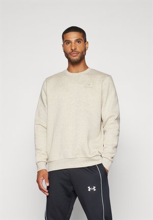 Sudadera de color beige claro con cuello redondo y puños acanalados. Presenta un logo sutil en el pecho, combinada con pantalones oscuros con rayas laterales.