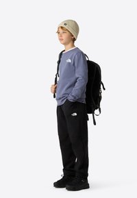 Felpa viola, pantaloni neri e un berretto lavorato a maglia crema. Zaino nero con cinghie regolabili. Presenta dettagli logo sull'abbigliamento.