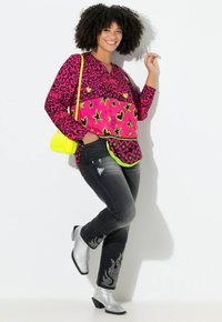 Blusa rosa brillante con estampado de leopardo, patrones de corazones y estrellas, combinada con jeans negros con detalles de llamas y botas de tobillo plateadas.
