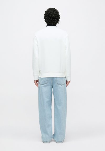 Sweatshirt branca com punhos e bainha canelados, combinada com jeans azul claro de corte largo com bolsos traseiros. Vista de costas.