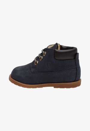 Bottine bleu marine pour tout-petit avec semelle marron, col noir rembourré et lacets rayés noir et blanc passés à travers des œillets dorés.