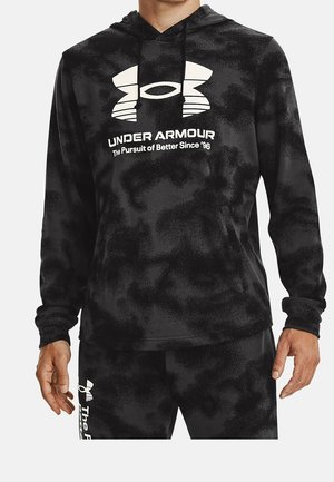 Mann trägt schwarzen Camo Under Armour Hoodie und passende Hose mit weißen Under Armour-Logos und Text.