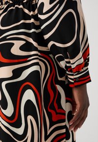 Vestido negro con remolinos abstractos en rojo, blanco y beige. Cuenta con un escote fruncido, mangas largas y puños abotonados. Textura de tela suave.