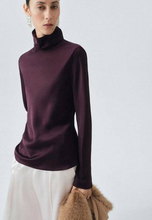 Haut en turtleneck violet en tissu lisse, design ajusté avec des manches longues, associé à une jupe de couleur claire et un accessoire en fourrure.