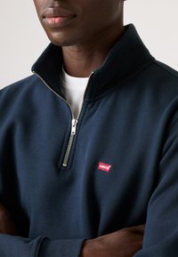Marineblauwe fleece half-rits pullover met een hoge kraag, zilveren rits en een klein rood Levi's logo op de borst. Zachte textuur.