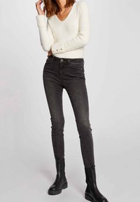 Zwarte skinny jeans met subtiele vervaging, gecombineerd met een zacht wit v-hals trui. Model draagt zwarte platform enkelboots.