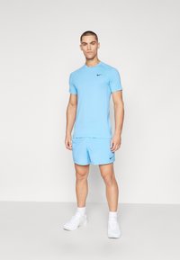 Lyseblå Nike trenings T-skjorte og matchende shorts med svarte logo aksenter. Stoffet virker glatt og fukttransporterende; hvite joggesko.
