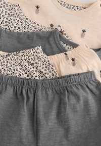 Trois paires de pyjamas pour bébé, une unie grise, une beige clair avec de petits ananas, et une à motif léopard.