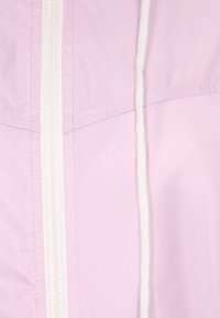 Giacca leggera di un rosa chiaro con una consistenza liscia, caratterizzata da una zip centrale e cordini bianchi. Le cuciture a punto evidenziano il design.