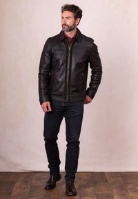 Brown leather jacket with a zip front, side pockets, and a slightly fitted design. Paired with dark jeans and brown leather boots.